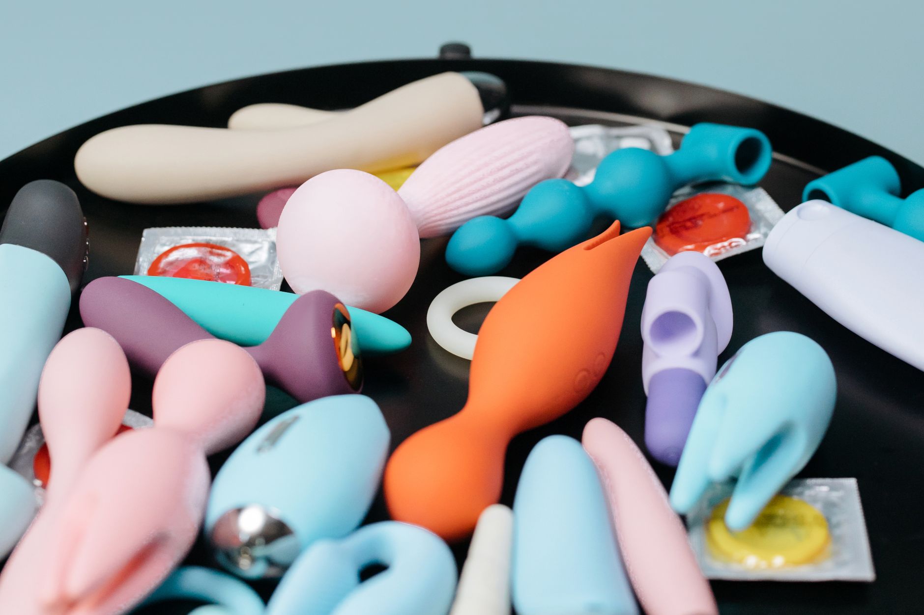 A collection of various colorful sex toys on a black surface, showing different shapes and designs for different preferences