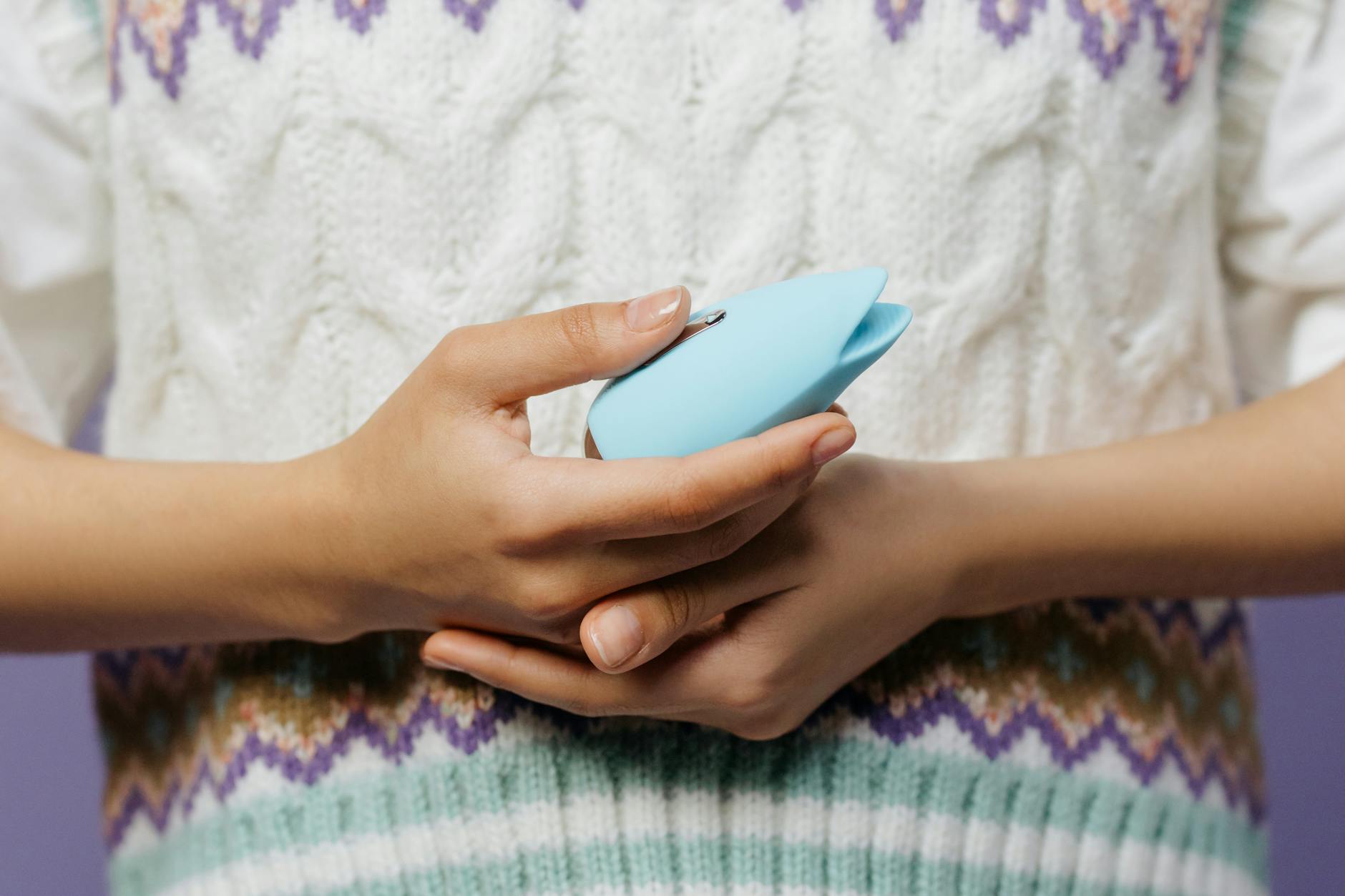 Close-up of hands holding a lemon vibrator against a knitted sweater during recovery.