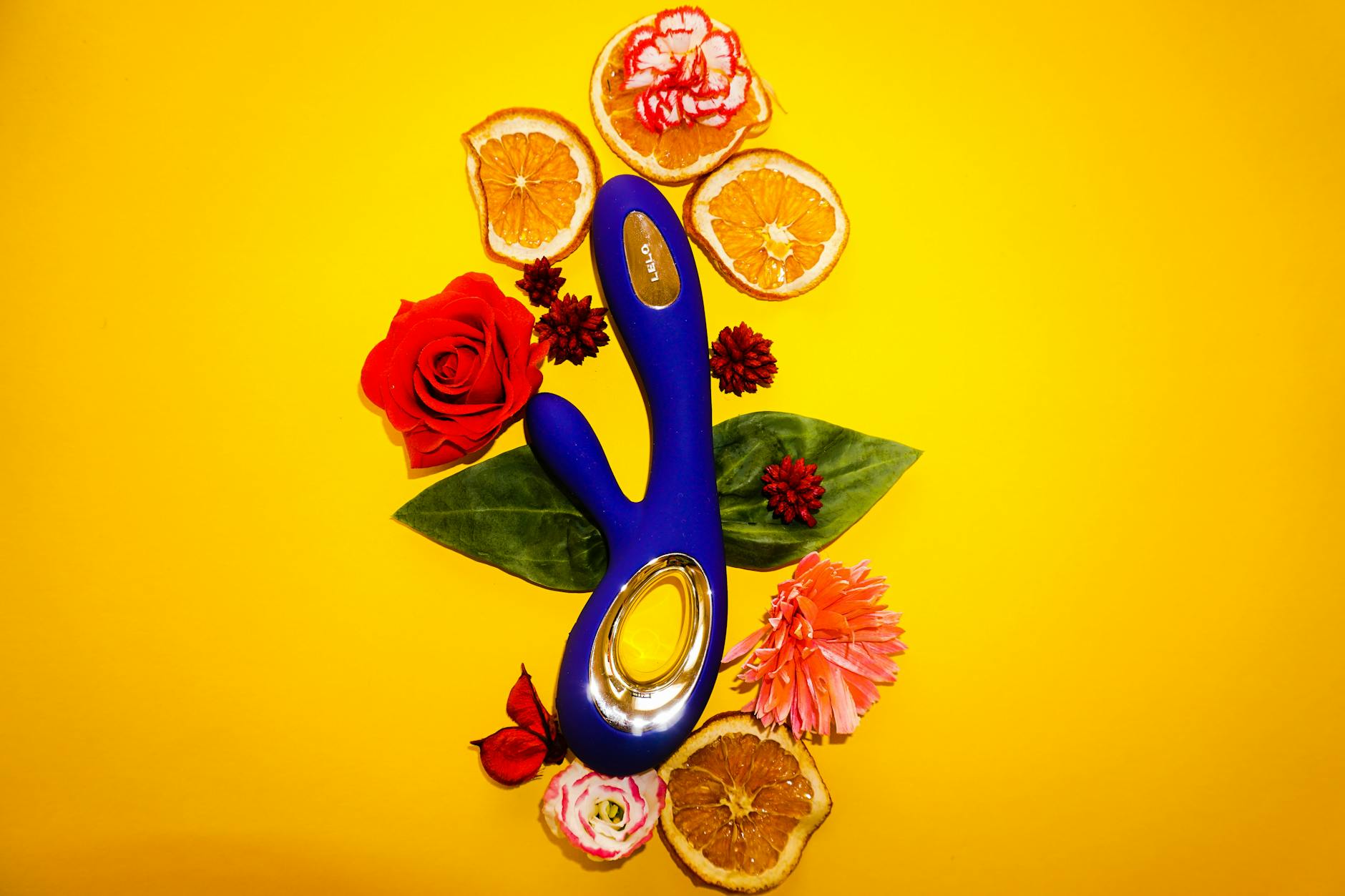 A blue lemon clitoral vibrator surrounded by fresh lemons and flowers on a bright yellow background.